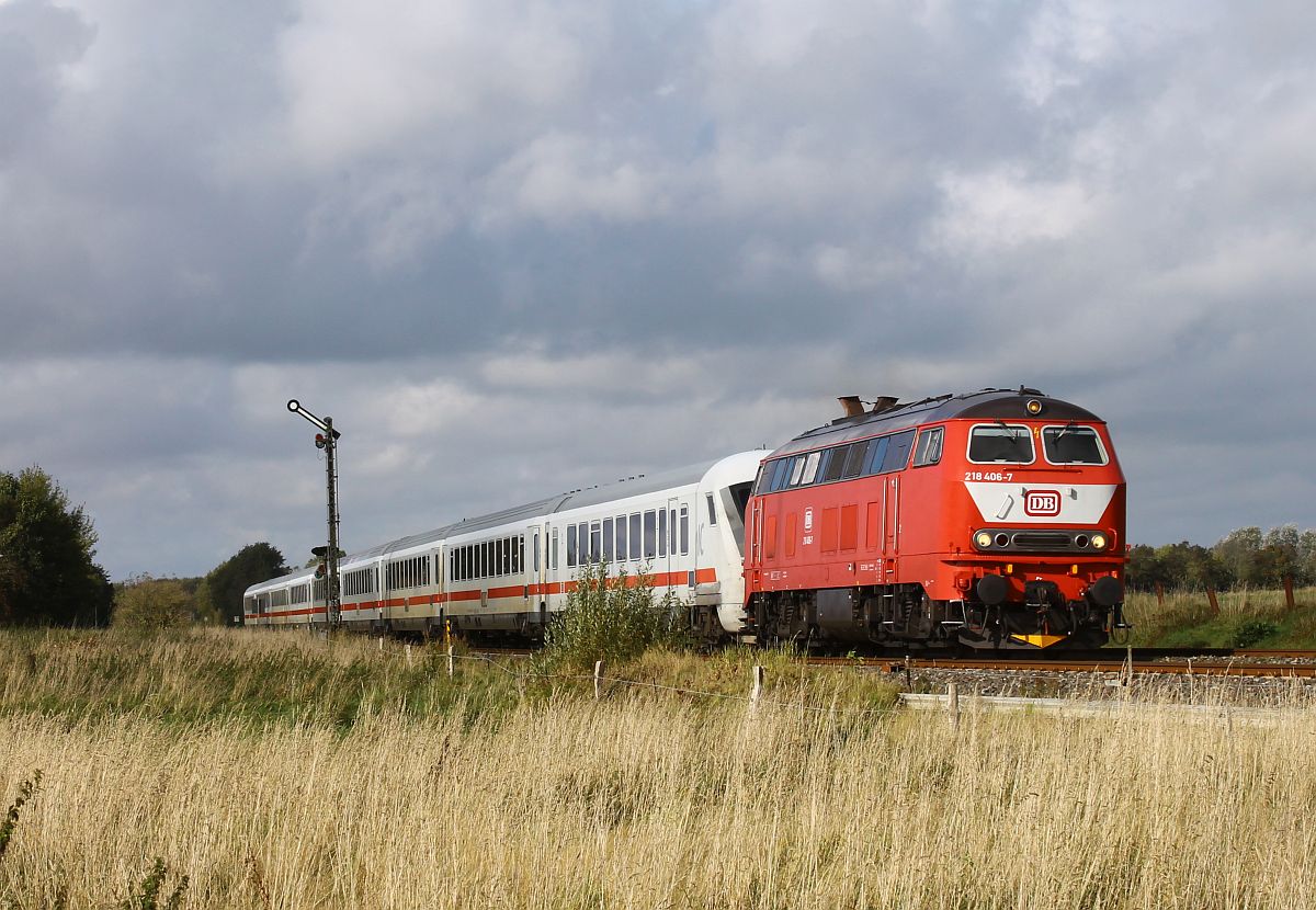 Die nach Niebüll verliehene orientrote 218 406 des Bw Kempten passiert vor dem IC 2215 das Einfahrtsignal von Lindholm am 09.10.2024